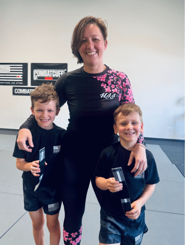 A coach poses with two young students proudly holding their CombatCuff rank anklets