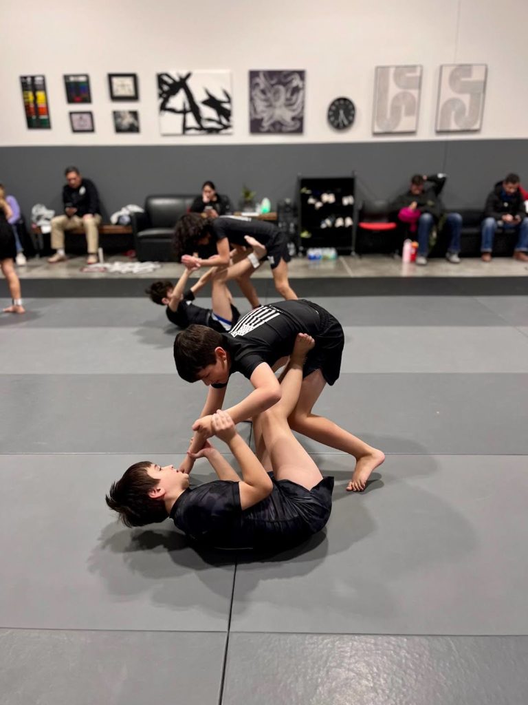 Niños practicando un derribo no-gi y un scramble con enredo de piernas
