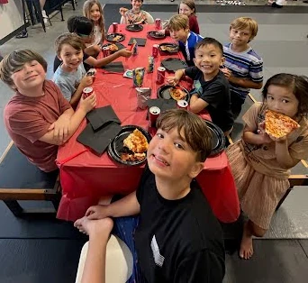 Kids sitting around a red party table with pizza on the mats at Heritage Jiu Jitsu