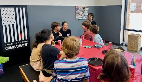 Kids and an adult sitting together at a red party table at Heritage Jiu Jitsu